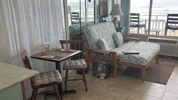 A room with a bed, a desk, and a chair. There is a view of the ocean through large windows.
