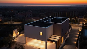 Een modern huis met een plat dak, een klein balkon en een goed verlichte ingang.