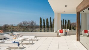 Een moderne buitenruimte met lounge stoelen, een eettafel en uitzicht op hoge bomen en een heldere lucht.