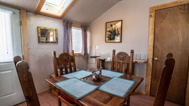 A cozy dining area with a wooden table and chairs, a skylight, a window with curtains, a mirror, and a door. - Stay in a historical mountain town! (Pitkin)