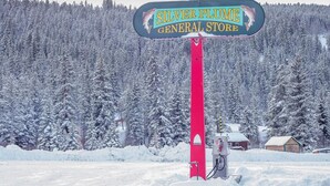 A sign for Silver Plume General Store with a red pole, set against a snowy forest backdrop. - Stay in a historical mountain town! (Pitkin)