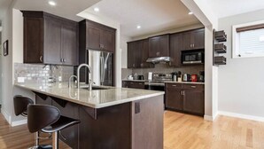 Une cuisine moderne avec des meubles de couleur bois foncé, des appareils en acier inoxydable et un îlot central doté de tabourets de bar.