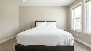 Une chambre à coucher avec un grand lit, une table de chevet et une fenêtre avec des stores.