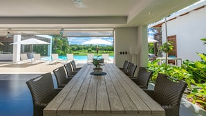 Una mesa de comedor de madera con sillas de mimbre, vista a una piscina y sombrillas exteriores.
