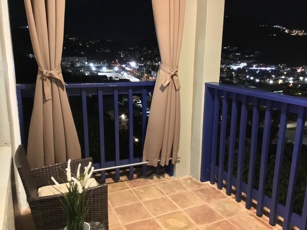 Enjoy the city view from this balcony with a wicker chair and a vase with fresh flowers.