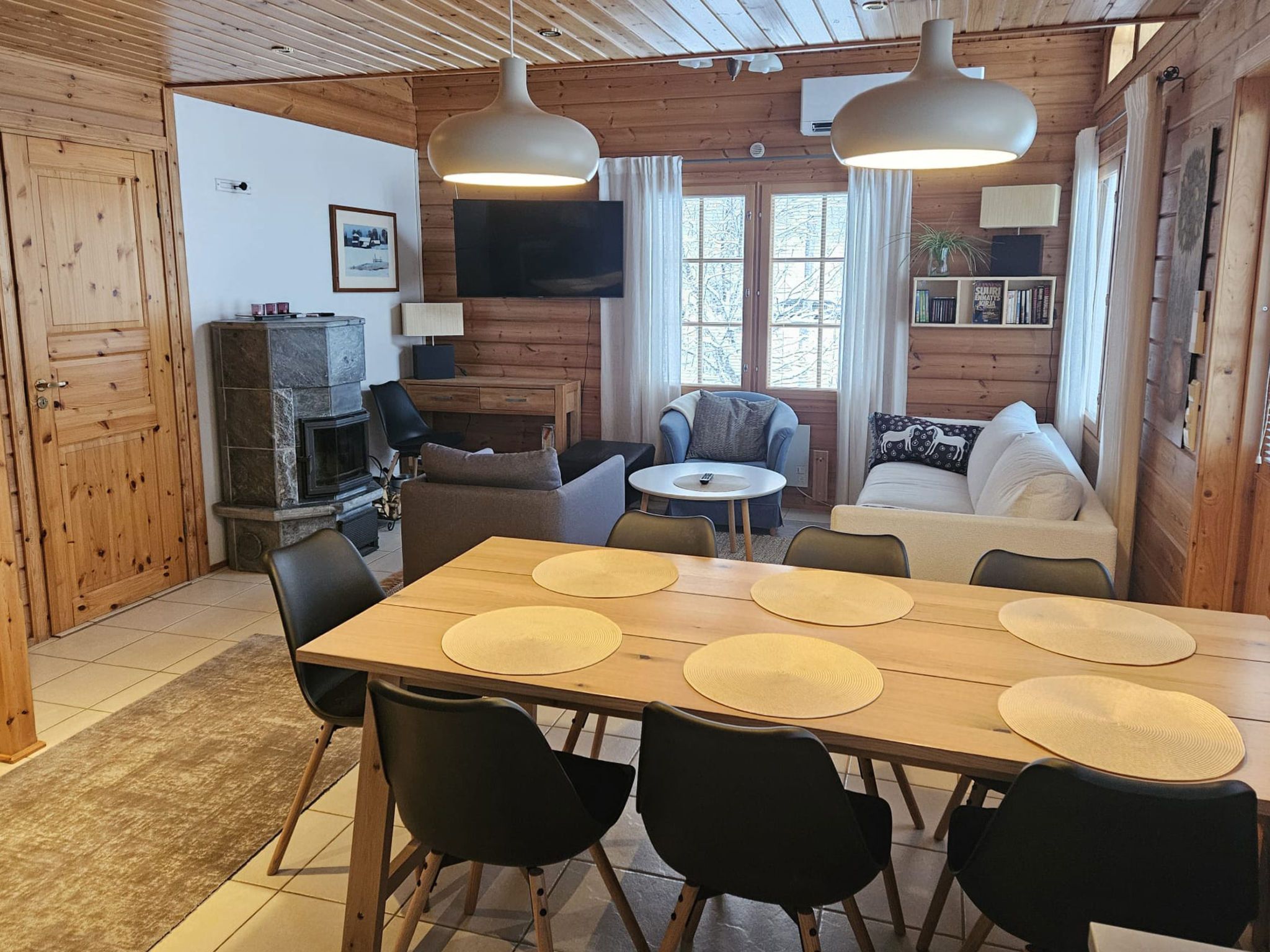 A cozy cabin interior with a dining table, chairs, a fireplace, a TV, and a sofa.