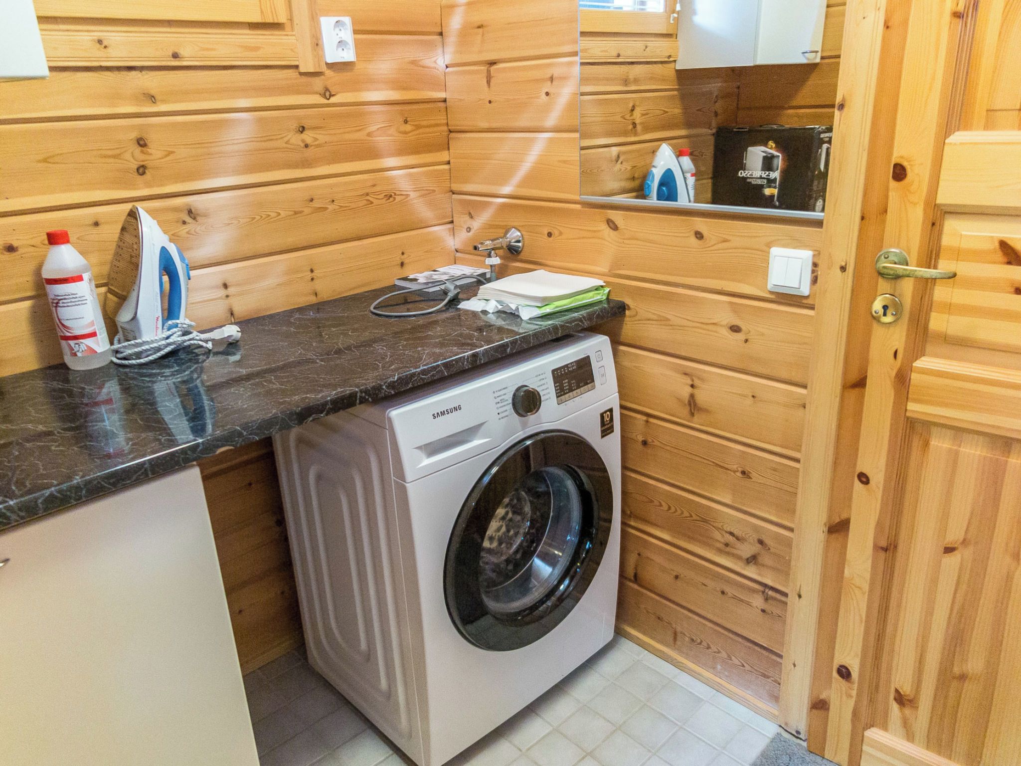 A compact kitchen with a washing machine, a countertop, and wooden walls.