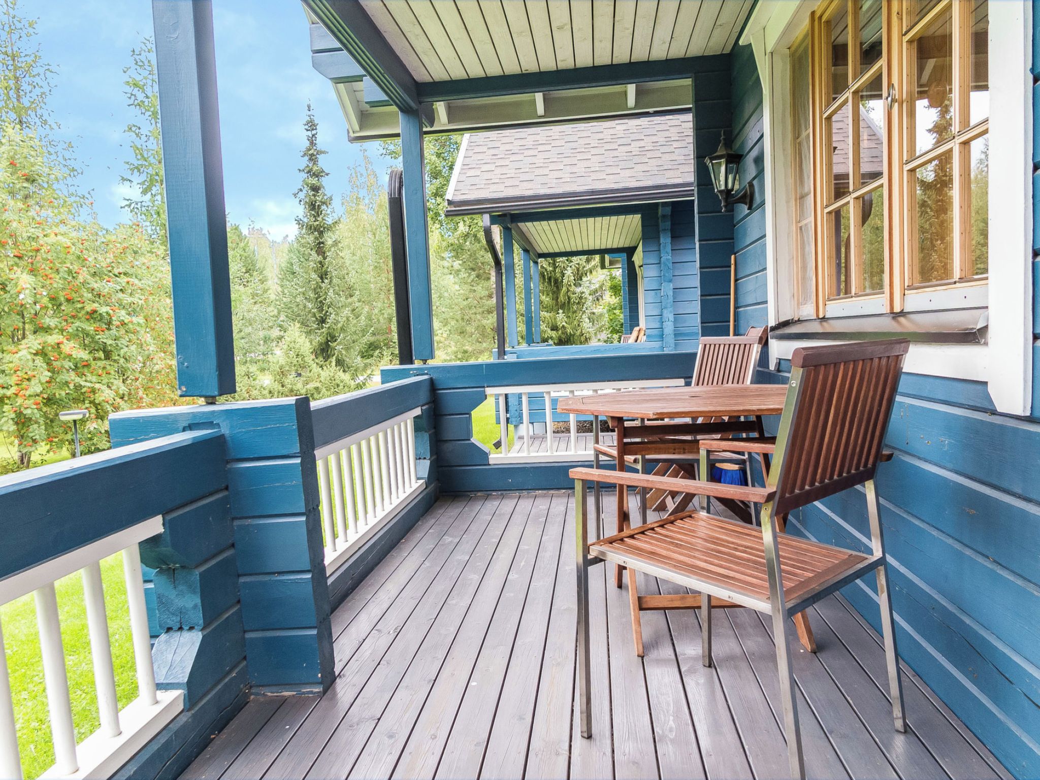 En træterrasse med et bord og stole, omgivet af et gelænder, med udsigt over et skovområde.