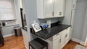 A modern kitchen with white cabinets, a black countertop, and a wooden floor. There is a welcome sign on the counter. - Remodeled Spacious Apartment in Perfect Location (Boston)