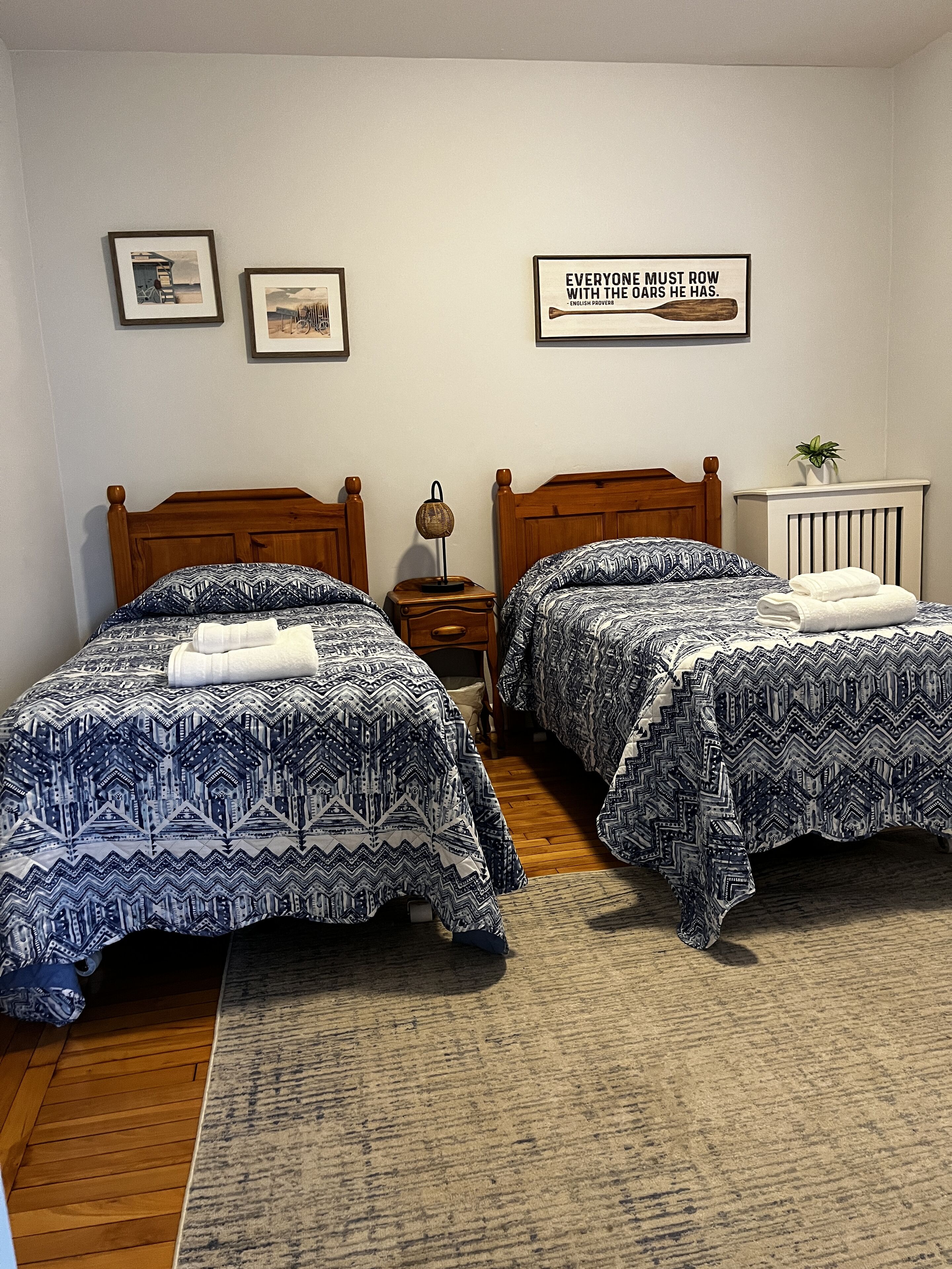 A bedroom with two beds, a nightstand, a wall-mounted lamp, and a framed quote.