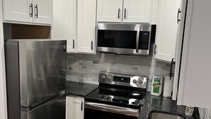 A modern kitchen with white cabinets, stainless steel appliances, a microwave, oven, and a sink. - Remodeled Spacious Apartment in Perfect Location (Boston)