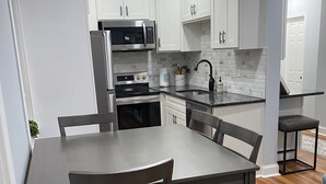 A modern kitchen with white cabinets, stainless steel appliances, and a wooden dining table with chairs. - Remodeled Spacious Apartment in Perfect Location (Boston)