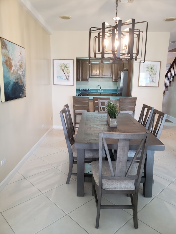 A dining area with a wooden table and chairs, a chandelier, and framed artwork on the walls. - Lagoon Luxury at Sandyport (Nassau)