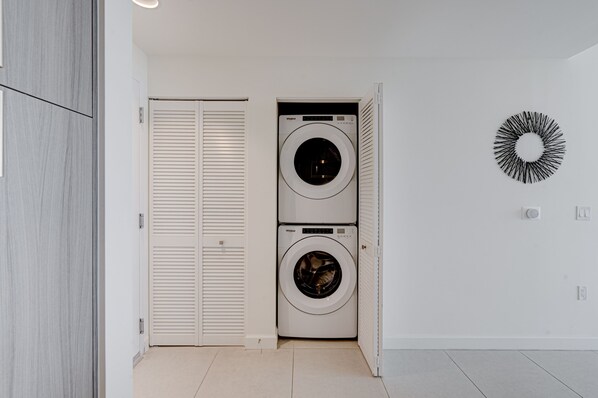A laundry room with two stacked washing machines, a white door, and a wall-mounted circular light fixture.