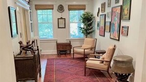 Una sala de estar con un sofá, sillones, una mesa de centro, un tapete y obras de arte en las paredes.