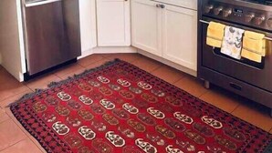 Una cocina con gabinetes blancos, una estufa de acero inoxidable y un tapete rojo estampado.