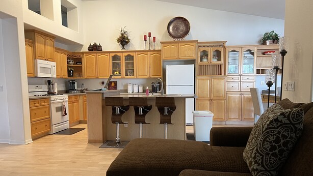 A modern kitchen with wooden cabinets, a central island with bar stools, a refrigerator, and a microwave. - Comfortable, clean, Spacious, relaxing home in metro-Phoenix area.🌵❤️🏡 (Chandler)