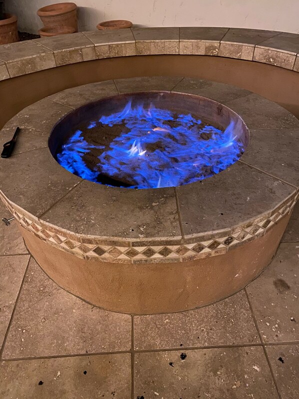 A circular stone fire pit with blue flames, surrounded by a tiled floor.