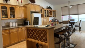 A modern kitchen with wooden cabinets, a central island, and a dining area with chairs. - Comfortable, clean, Spacious, relaxing home in metro-Phoenix area.🌵❤️🏡 (Chandler)