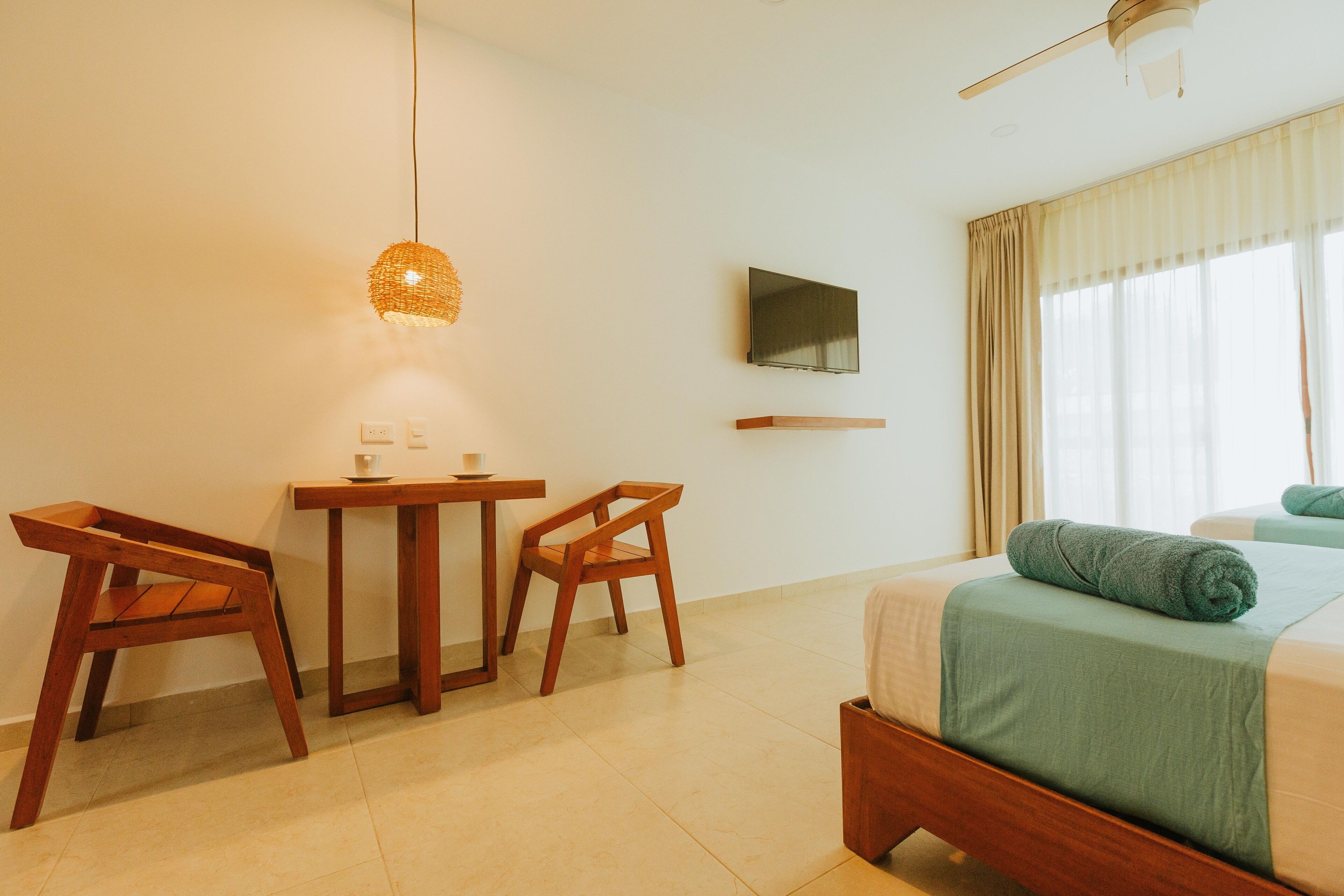 A hotel room with a bed, a desk with chairs, a television on the wall, and a window with curtains.