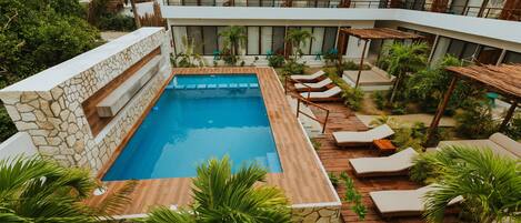 Un área de piscina con sillas de descanso, un muro de piedra y una construcción con techo de paja.