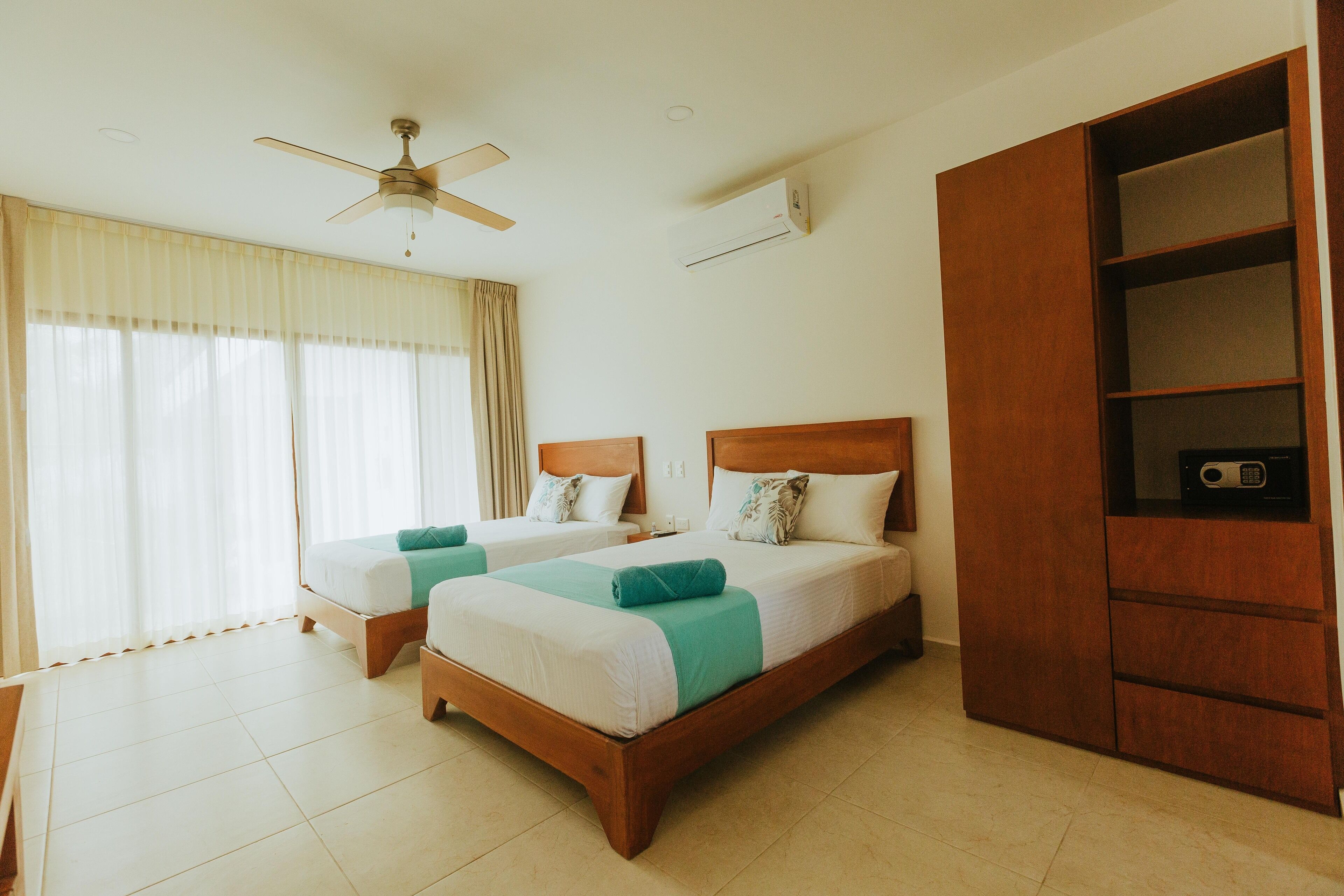 Une chambre d’hôtel avec deux lits, un ventilateur de plafond, un appareil de climatisation et une armoire en bois.