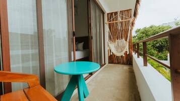 A balcony with a wooden table and bench, a hanging macrame chair, and a view of greenery.