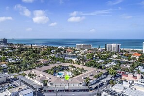 An aerial view of a coastal city with a prominent hotel featuring a rooftop pool and a view of the ocean.