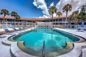 A pool area with lounge chairs and palm trees, surrounded by a building with a white fence.