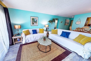 A living room with two white sofas, a coffee table, and a rug. There are wall art pieces and a clock. - Steps from St. Armands! Walk to Beach, Heated Pool (Sarasota)