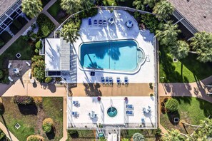 An aerial view of a hotel with a large swimming pool surrounded by lounge chairs and umbrellas, a covered patio area, and lush landscaping. - Walk to Lido Beach & Steps to St. Armand's Circle | Heated Pool and Spa | BBQ (Sarasota)