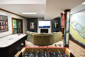 A living room with a foosball table, a fireplace, a large TV, and a couch.