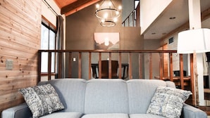 Ein modernes Interieur mit einem grauen Sofa, Holzwänden, einer Treppe und einem Chandelier.