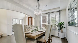 A dining area with a wooden table set for four, upholstered chairs, a chandelier, and a potted plant. - Elegant spacious home with water view. Prime location- Richmond, Katy, Houston, Rosenberg. (Richmond)