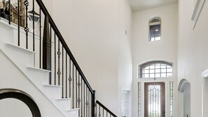 A spacious hallway with a dark wooden floor, white walls, and a black staircase with decorative railings. - Elegant spacious home with water view. Prime location- Richmond, Katy, Houston, Rosenberg. (Richmond)
