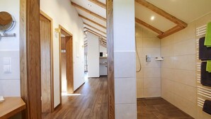 A hallway with wooden flooring and a door, leading to a bathroom with a tiled shower and a towel rack with multiple towels. - Vacation apartment Schwalbennest (Chieming)