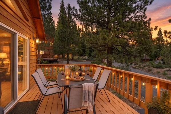 A wooden deck with a table and chairs, surrounded by a railing, overlooking a forested area.