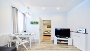 Un salon moderne comprenant un coin repas, un téléviseur et un couloir menant à une chambre.