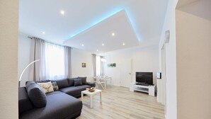 Un salon moderne avec un canapé gris, une petite table blanche et un téléviseur à écran plat.