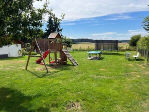 A grassy backyard with a wooden play structure, a table, and chairs. - Vacation apartment 2 - Wiedemann Heiko (Dargen)