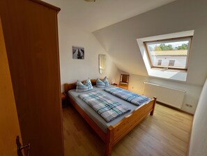 Quarto com cama de madeira, claraboia, radiador e uma pequena mesa.