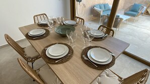 Comedor con una mesa de madera dispuesta para seis personas, rodeada de sillas de mimbre con cojines.