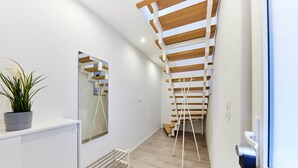 A modern interior with a white wall, a wooden slatted ceiling, a potted plant, a radiator, and a door with a handle.