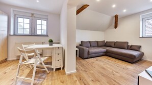 A modern living room with a wooden floor, a grey sectional sofa, a white desk with a chair, and a radiator.
