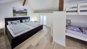 A bedroom with a large bed, a bunk bed, wooden beams, a window, and a painting on the wall.