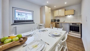 A modern kitchen with white cabinets, a built-in oven, and a dining area set for four with white tableware and fruit.