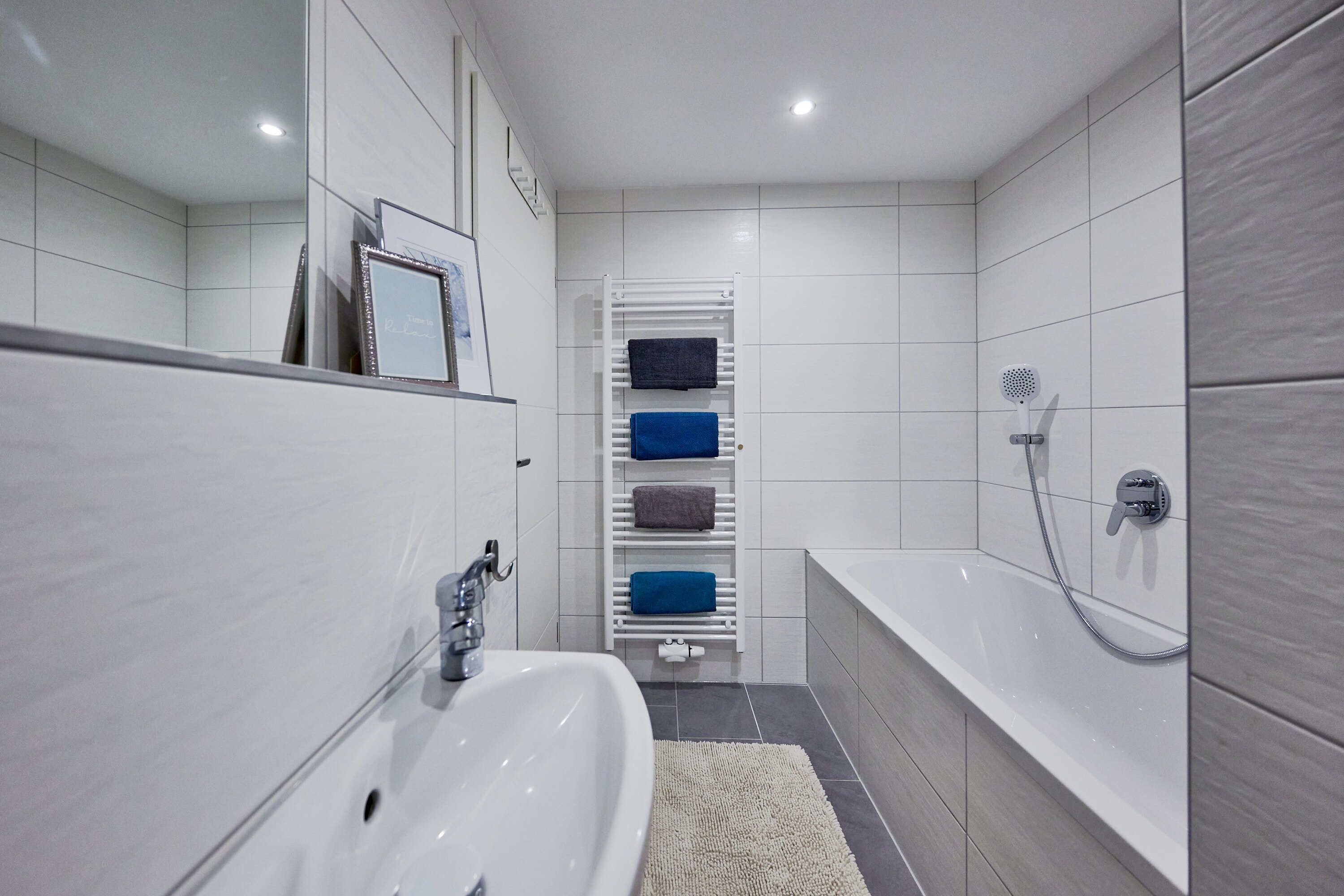 Ein modernes Badezimmer mit einem weißen Waschbecken, einer Badewanne und einem Handtuchhalter mit mehreren Handtüchern.