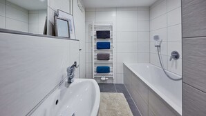 A modern bathroom with a white sink, a bathtub, and a towel rack with multiple towels.