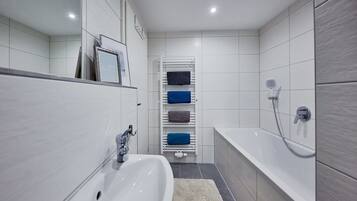 Ein modernes Badezimmer mit einem weißen Waschbecken, einer Badewanne und einem Handtuchhalter mit mehreren Handtüchern.