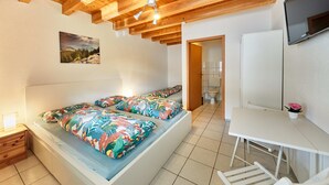 A bedroom with a bed, bedside table, and a desk with a chair. - Schönes Zimmer mit Bad - nur 10 Gehminuten vom Europa-park (Rust)
